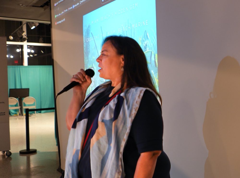 Miami Beach Commissioner Laura Dominguez speaks at the Spring 2025 Reef Town Hall, a &lsquo;Creating the Miami Beach Marine Park&rsquo; slide projected behind her